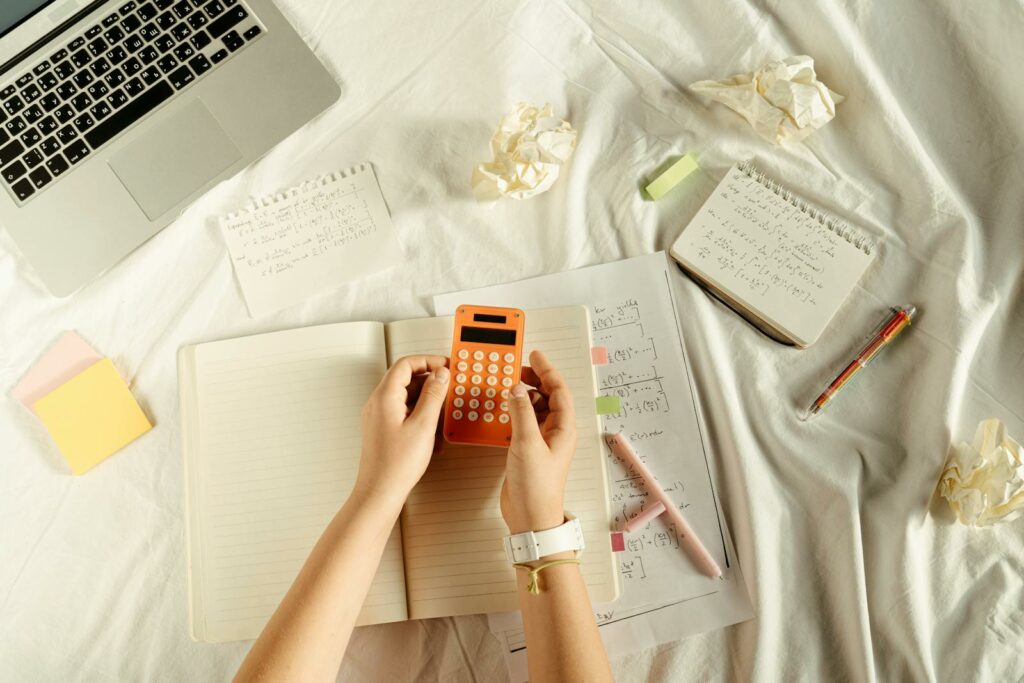 Flat lay of hands with orange calculator, notes, and laptop in a learning setting.