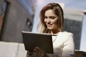 A woman joyfully using a digital tablet outdoors in the city during the day.