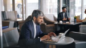 Businessman working on a laptop in a modern café setting, focused on tasks.