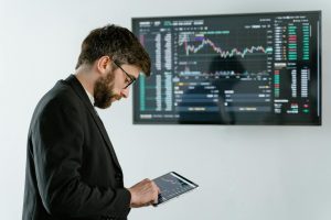 Professional man using tablet in front of cryptocurrency trading screen indoors.
