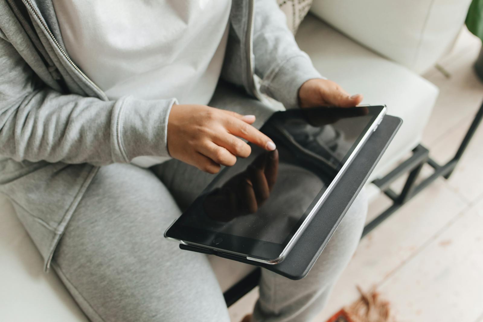 Close-up of a person interacting with a tablet indoors, wearing casual clothing, emphasizing modern technology use.